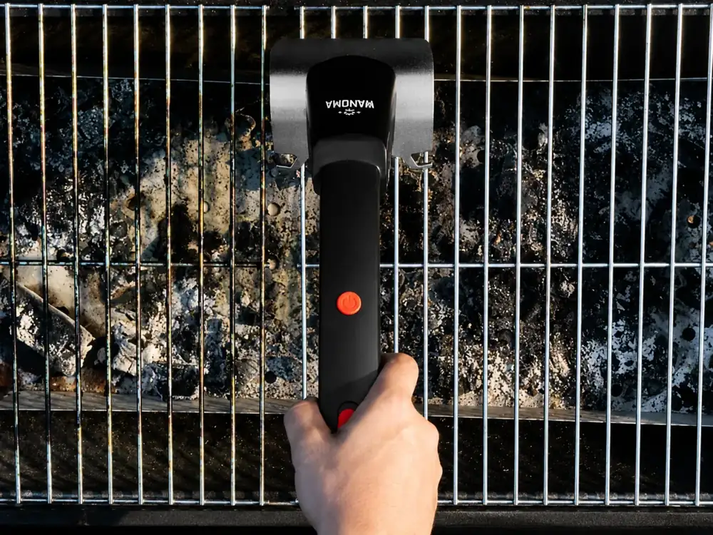Cordless Wamoma GrillMaster cleaning a fired-up charcoal grill